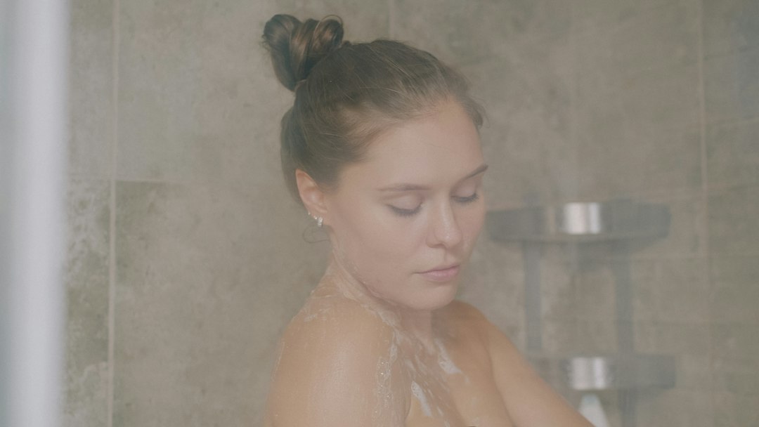 A woman with hair in a bun washing in a steamy tiled shower